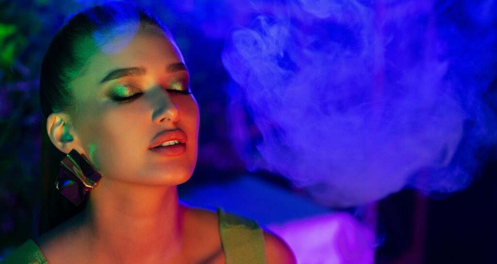 Young woman smoking vape in neon blue light